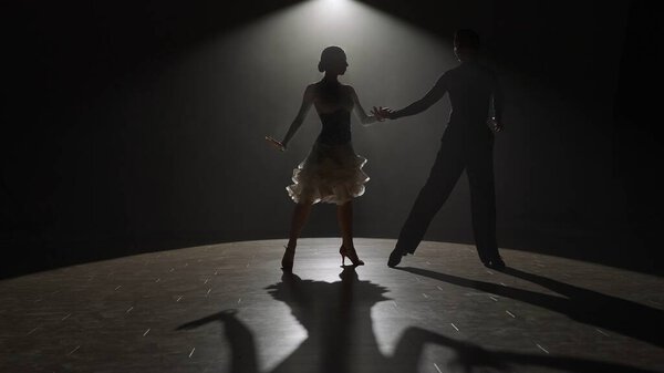 Бальная танцевальная пара Elegant на Spotlight. Это поразительное изображение запечатлевает танцевальную пару во время спектакля, окутанную в сингулярное освещение против темноты, подчеркивая их форму и