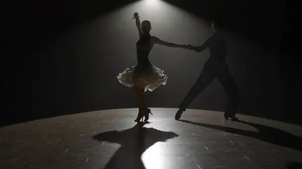 Elegant Ballroom Dance Couple on Spotlight. This striking image captures a ballroom dancing couple mid-performance, enveloped in a singular spotlight against the darkness, highlighting their form and