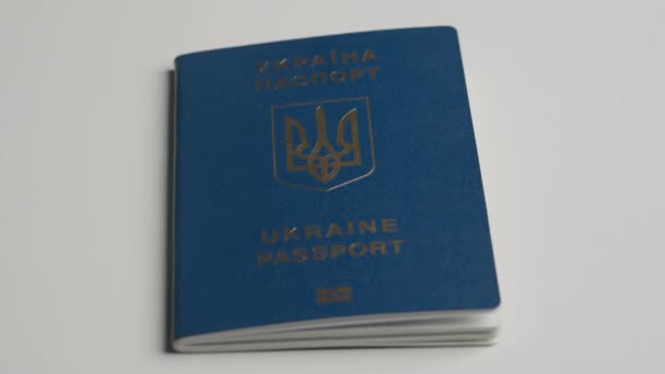 パスポートと移行クリエイティブ広告コンセプト 人物の身元を証明する書類を閉じます ウクライナのパスポートは ホワイトテーブルの上に横たわっており これは手で奪われます — ストック動画