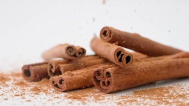 Aromatik baharatlar yaratıcı reklam konsepti. Yemek malzemelerinin stüdyo çekimlerini kapat. Beyaz arka planda, üzerine tarçın tozu dökülmüş kahverengi tarçın çubukları yığını var..