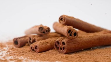 Aromatik baharatlar yaratıcı reklam konsepti. Yemek malzemelerinin stüdyo çekimlerini kapat. Kahverengi kurutulmuş tarçın çubukları beyaz zemine serilmiş toz ve tepeden düşen birkaç çubuk..