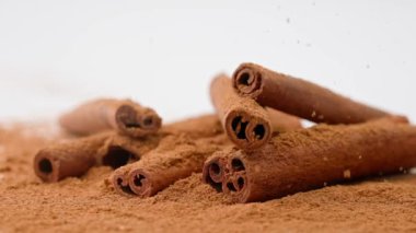 Aromatik baharatlar yaratıcı reklam konsepti. Yemek malzemelerinin stüdyo çekimlerini kapat. Kahverengi kurutulmuş tarçın çubukları beyaz zemine serilmiş toz ve tepeden düşen birkaç çubuk..