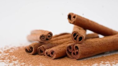 Aromatik baharatlar yaratıcı reklam konsepti. Yemek malzemelerinin stüdyo çekimlerini kapat. Kahverengi kurutulmuş tarçın çubukları beyaz zemine serilmiş toz ve tepeden düşen birkaç çubuk..