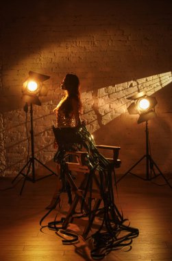 Film seti ve sahne arkası yaratıcı reklam konsepti. Çekici kadın oyuncu portresi. Altın elbiseli güzel bir kadın yönetmen koltuğunun yanında duruyor elinde film makarası yerde yatıyordu..