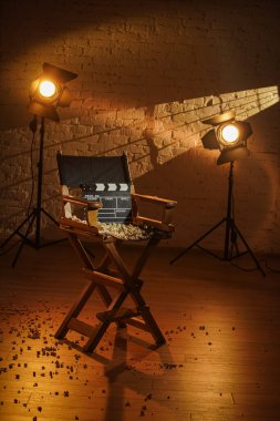 Film seti ve sahne arkası yaratıcı reklam konsepti. Sinemanın yakın plan çekimleri yönetmen koltuğunda dikilirken patlamış mısır etrafa saçılmış, arka plandaki spot ışıklarından gelen ışıklar....