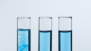 Beyaz arka planda üç cam test tüpü. Test tüpleri mavi sıvıyla dolu, biri mavi çözünen bir madde gösteriyor. Tıp kavramı, biyokimyasal araştırma. Yakın plan.