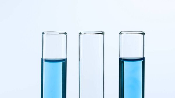 Three glass test tubes on a white background. Two test tubes are filled with blue liquid and one is empty. Concept of medicine, biochemical research. Close-up