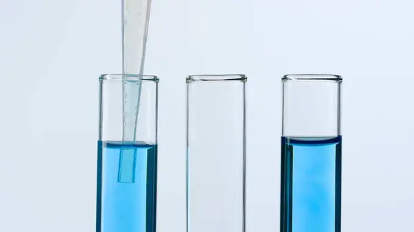 Three glass test tubes on a white background. Two test tubes are filled with blue liquid and a pipette is lowered into one of them. Concept of medicine, biochemical research. Close-up