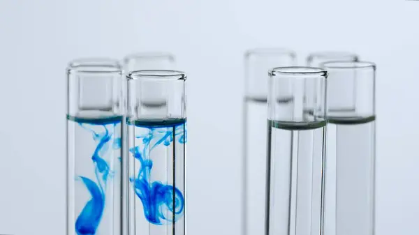 Science and biotechnology creative concept. Close-up of laboratory glassware on white background. Test tubes with transparent liquid and dissolving cloud of blue substance
