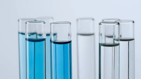 Science and biotechnology creative concept. Close up shot of laboratory glassware on white background. Test tubes with transparent and blue liquid fluid in laboratory, scientific expertise