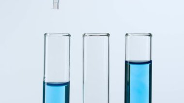 Bilim ve biyoteknoloji kavramı işte. Beyaz arka planda laboratuvar aletlerinin yakın plan görüntüleri. İçinde mavi bir maddenin plastik bir pipetten damladığı mavi sıvılı tüpler. Yavaş çekim