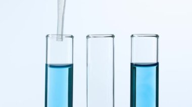 Bilim ve biyoteknoloji kavramı. Beyaz arka planda laboratuvar camlarının yakın plan görüntüsü. Mavi sıvıyla dolu test tüplerinin stüdyo çekimi. Bilim adamı tüpten sıvı pipetler. Yavaş çekim.