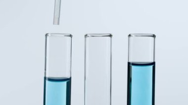 Bilim ve biyoteknoloji kavramı işte. Beyaz arka planda laboratuvar aletlerinin yakın plan görüntüleri. İçinde mavi bir maddenin plastik bir pipetten damladığı mavi sıvılı tüpler. Yavaş çekim
