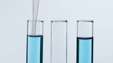 Bilim ve biyoteknoloji kavramı işte. Beyaz arka planda laboratuvar aletlerinin yakın plan görüntüleri. Numunelerin plastik bir pipetle alındığı mavi sıvılı tüpler. Yavaş çekim