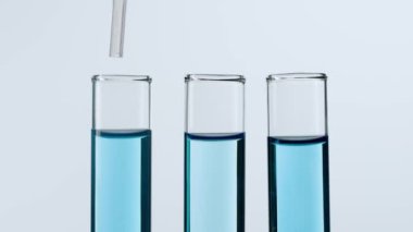 Bilim ve biyoteknoloji kavramı. Beyaz arka planda laboratuvar camlarının yakın plan görüntüsü. Mavi sıvıyla dolu test tüplerinin stüdyo çekimi. Bilim adamı tüpten sıvı pipetler. Yavaş çekim.