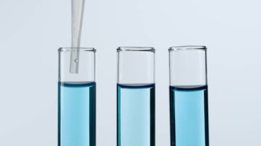 Bilim ve biyoteknoloji kavramı. Beyaz arka planda laboratuvar camlarının yakın plan görüntüsü. Mavi sıvıyla dolu test tüplerinin stüdyo çekimi. Bilim adamı tüpten sıvı pipetler. Yavaş çekim.