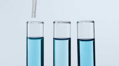 Bilim ve biyoteknoloji kavramı işte. Beyaz arka planda laboratuvar aletlerinin yakın plan görüntüleri. Numunelerin plastik bir pipetle alındığı mavi sıvılı tüpler. Yavaş çekim.