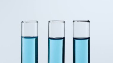 Bilim ve biyoteknoloji kavramı. Beyaz arka planda cam bardakları kapatın. Renkli sıvılarla dolu test tüplerinin stüdyo çekimi, bilim adamı tüpün içine mavi mürekkep sıvısı ekledi. Yavaş çekim.