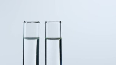 Bilim ve biyoteknoloji kavramı. Beyaz arka planda cam bardakları kapatın. Stüdyo çekiminde şeffaf sıvıyla dolu deney tüpleri kullanıldı. Bilim adamı pipeti tüpe sokup çıkardı. Yavaş çekim
