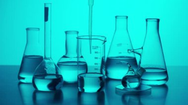 Bilim ve biyoteknoloji yaratıcı kavramı. Bir sürü farklı deney tüpü ve matarası olan laboratuvar masası analiz için tüpten sıvı alan bilim adamı pipetleri, yakın plan mavi neon. Yavaş çekim.