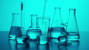 Bilim ve biyoteknoloji yaratıcı kavramı. Laboratuvar masasında farklı deney tüpleri ve mataralar var. Bilim adamı pipetleri tüp içinde sıvı damlalar, mavi neon arka plan kapalı. Yavaş çekim.