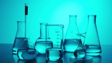 Bilim ve biyoteknoloji yaratıcı kavramı. Mavi arka plandaki cam örtüyü kapat. Laboratuvar masasında deney için bir sürü deney tüpü ve sıvıyla dolu mataralar var. Mavi neon ışığı. Yavaş çekim.