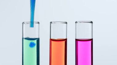 Bilim ve biyoteknoloji kavramı işte. Beyaz arka planda laboratuvar aletlerinin kapatılması. Test tüpleri pembe, yeşil, kırmızı sıvıyla dolu. Bilim adamı deney tüpünden mavi sıvı çıkarıyor. Yavaş çekim