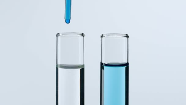 科学和生物技术的概念 白底实验室器具的特写 用透明液体将蓝色物质滴入试管中 慢动作 — 图库视频影像