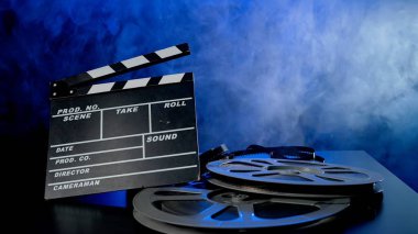 El çırpma tahtası ve mavi neon ışıkta duman bulutları içinde film makaraları. Film yapma kavramı