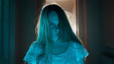 Korku filmi ve kötü ruh yaratıcı reklam konsepti. Evde hayalet kadın portresi var. Beyaz elbiseli, korkunç yüzlü, poz veren ve kameraya bakan bir kadın..