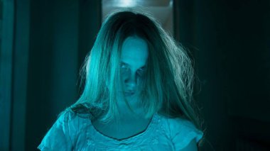 Korku filmi ve kötü ruh yaratıcı reklam konsepti. Evde hayalet kadın portresi var. Beyaz elbiseli, korkunç yüzlü, poz veren ve kameraya bakan bir kadın..