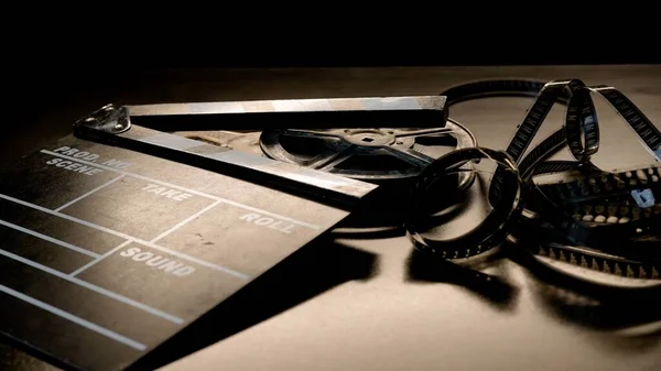 クラッパーボードとスポットライトのビームにフィルムロールのリール ブラックバックのスタジオでの映画産業機器 — ストック写真