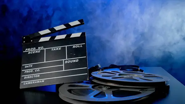 Clapper board and reels with film in clouds of smoke in blue neon light. Concept of film making