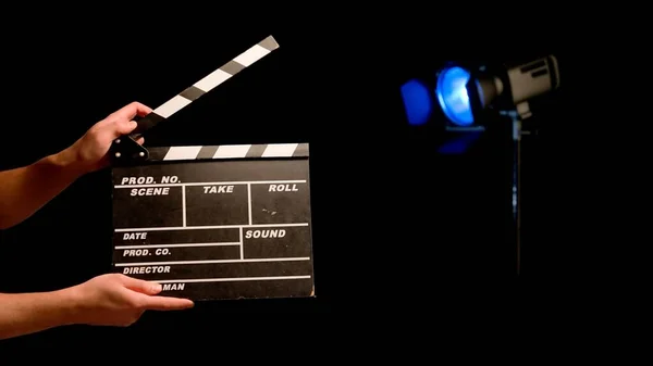 Directors assistant holding movie clapper on filming location. A film clapper in the hands of assistant director in a studio on a black background, illuminated by a spotlight with blue neon light