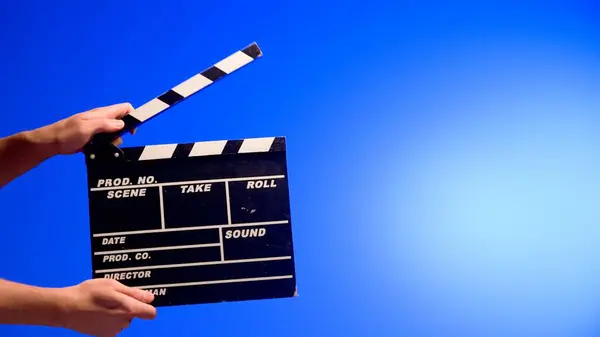 Hand is holding Black clapper board or movie slate on a blue background with a circular light. Cinema industry, entertainment