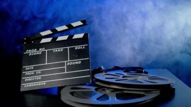 El çırpma tahtası ve mavi neon ışıkta duman bulutları içinde film makaraları. Film yapma kavramı