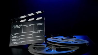 Tahta bir alkış tahtası ve ahşap bir masanın üzerinde bir makara film makarası. Stüdyoda film endüstrisi envanteri siyah arka planda mavi neon ışığı altında