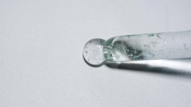 Sıvı ve jel yaratıcı reklam konsepti. Beyaz arkaplandaki saydam maddenin yakın çekim görüntüsü. Cam pipette temiz yüzeye kozmetik ürün jel sıvısı ya da serum dökülüyor. Yavaş çekim.