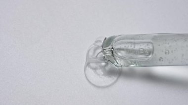 Sıvı ve jel yaratıcı reklam konsepti. Beyaz arkaplandaki saydam maddenin yakın çekim görüntüsü. Cam pipet yüzeyine kozmetik ürün jel sıvısı kabarcıkları döker. Yavaş çekim.