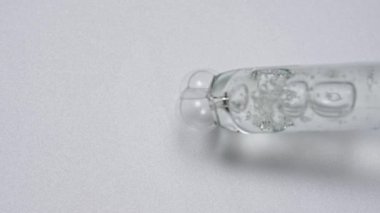 Sıvı ve jel yaratıcı reklam konsepti. Beyaz arkaplandaki saydam maddenin yakın çekim görüntüsü. Cam pipet yüzeyine kozmetik ürün jel sıvısı kabarcıkları döker. Yavaş çekim.