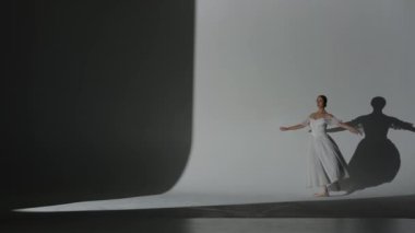 Klasik ve modern bale yaratıcı reklam konsepti. Stüdyoda sahne ışıkları altında beyaz arka plandaki kadın portresi. Beyaz tül içinde güzel bir balerin koreografinin elementini gösteriyor..