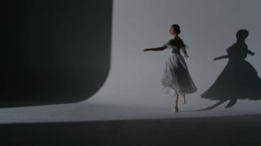 Klasik ve modern bale yaratıcı reklam konsepti. Stüdyoda sahne ışıkları altında beyaz arka plandaki kadın portresi. Beyaz tüller içinde güzel bir balerin dans ederek koreografinin hareketlerini çeviriyor..