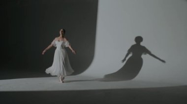 Klasik ve modern bale yaratıcı reklam konsepti. Stüdyoda sahne ışıkları altında beyaz arka plandaki kadın portresi. Beyaz tül içinde güzel bir balerin dans ederek koreografinin atlama hareketlerini yapıyor..