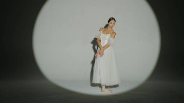 Klasik ve modern bale yaratıcı reklam konsepti. Stüdyoda parlak bir spot ışığı altında beyaz arka plandaki kadın portresi. Beyaz tül içinde dans eden zarif balerin, yüksek oranda parçalanmış elementi gösteriyor..