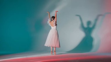 Klasik ve modern bale yaratıcı reklam konsepti. Pembe ışıklı stüdyoda yeşil arka planda bir kadının portresi. Beyaz tüllü genç balerin koreografinin güzel bir unsurunu gösteriyor..