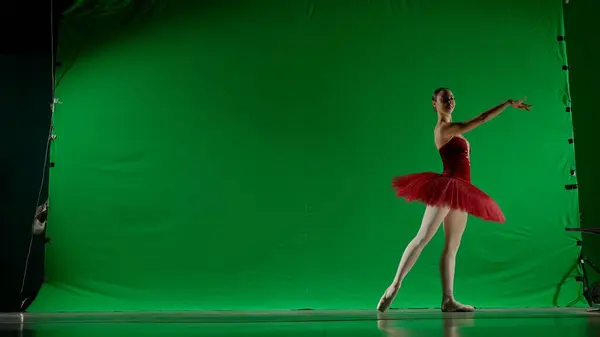 Classical and modern ballet creative advertising concept. Woman on chroma key background of green screen. Beautiful ballerina in red tutu and pointe shoes dancing choreography in studio.