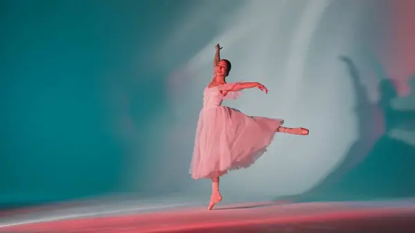 Classical and modern ballet creative advertisement concept. Portrait of female on green background in pink neon light studio. Young ballerina in white tulle showing beautiful element of choreography.