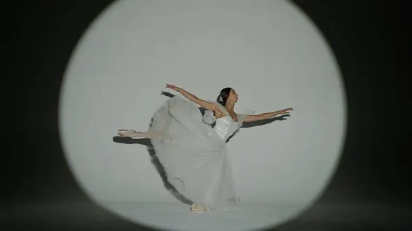 Classical and modern ballet creative advertisement concept. Portrait of female on white background in studio in bright spotlight. Elegant ballerina in white tulle dancing showing high split element.