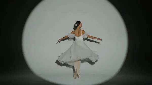Classical and modern ballet creative advertisement concept. Portrait of female on white background in studio in bright spotlight. Elegant ballerina in white tulle dancing showing high split element.
