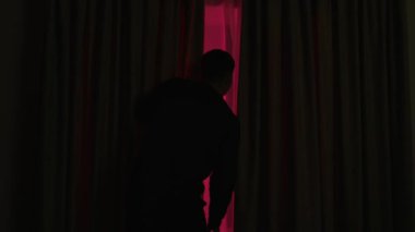 Pencerenin dışında neler olduğunu görmek için karanlık bir odada perdeleri açan bir adamın arka görüntüsü. Polis ışıklarına bakan bir adam.